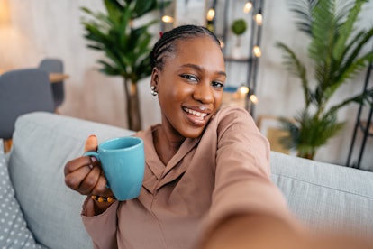 Young beautiful black smiling woman relaxing on sofa at her home and taking selfies.