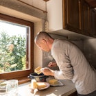 A man in a white long sleeve tee is leaning over a kitchen counter with a few slabs of butter