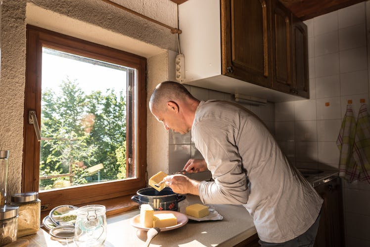 A man in a white long sleeve tee is leaning over a kitchen counter with a few slabs of butter