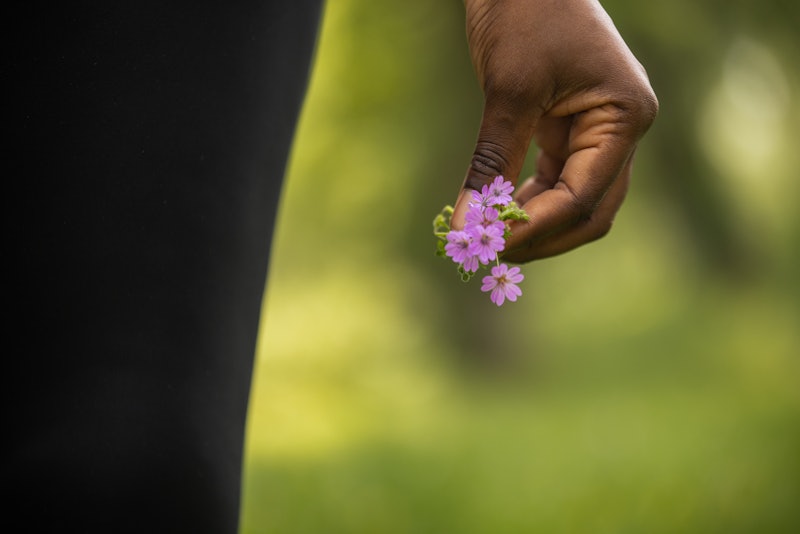 Young Black woman holding a pink flower in a forest