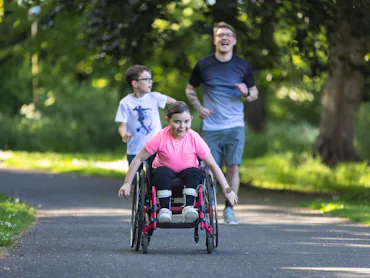 A young girl who is a wheelchair user, riding fast along a path in a public park in Newcastle Upon T...