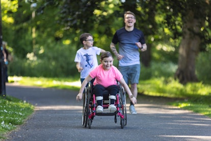 A young girl who is a wheelchair user, riding fast along a path in a public park in Newcastle Upon T...