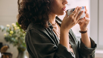 A side view of an unrecognizable serious Caucasian female enjoying drinking her morning coffee at ho...