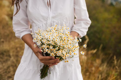 Summer outdoors portrait of faceless young woman wearing cotton white dress holding big bunch of whi...