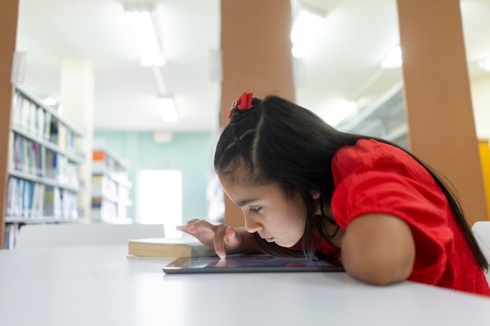 A shortsighted little latin girl using a digital tablet with her face close to the screen.