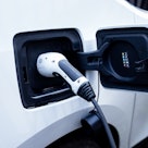 Photo of white electric vehicle with power plug inserted into charging socket during charging sessio...