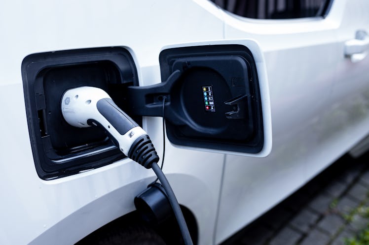 Photo of white electric vehicle with power plug inserted into charging socket during charging sessio...