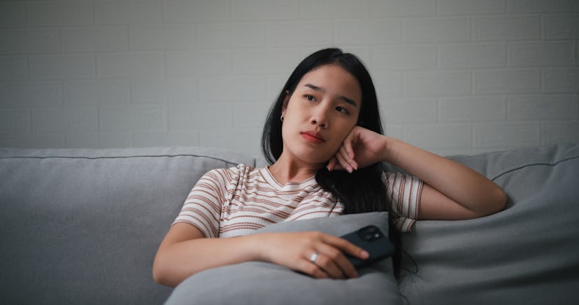 Portrait of Unhappy young Asian woman feeling bored or Sad while using a smartphone sitting on the c...