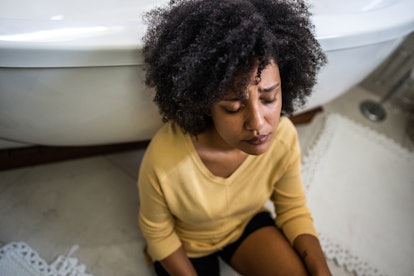 Sad young woman sitting on ground in the bathroom at home