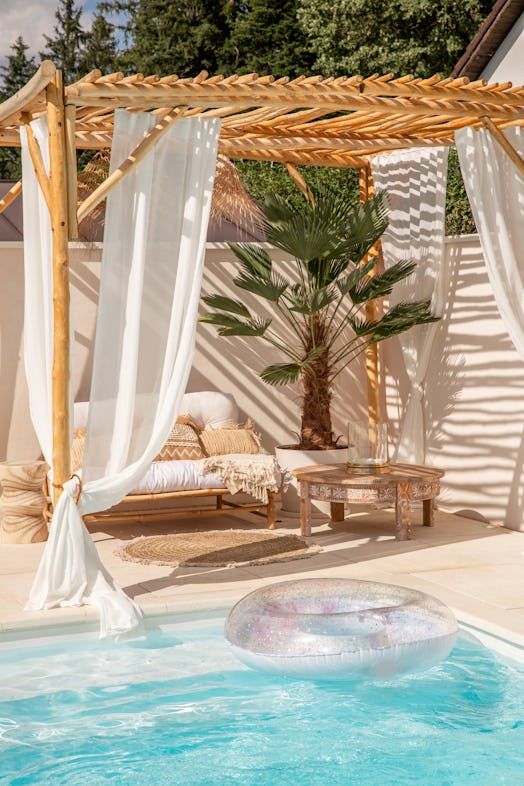 Boho bamboo outdoor sofa under driftwood pergola by the swimming pool in warm sunlight