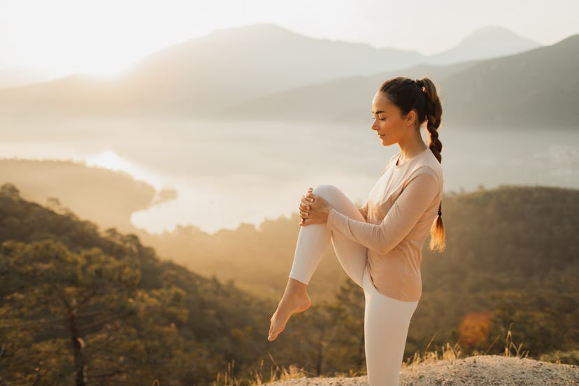 Young athletic woman practicing yoga by the nature with amazing mountain view at sunset or sunrise. ...