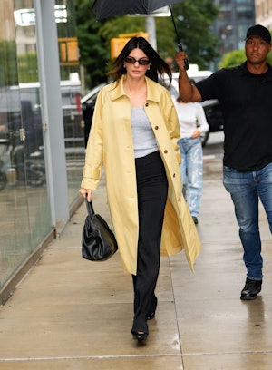 Kendall Jenner wears a tank, trousers, yellow coat, and massive black bag on September 18, 2023 in N...