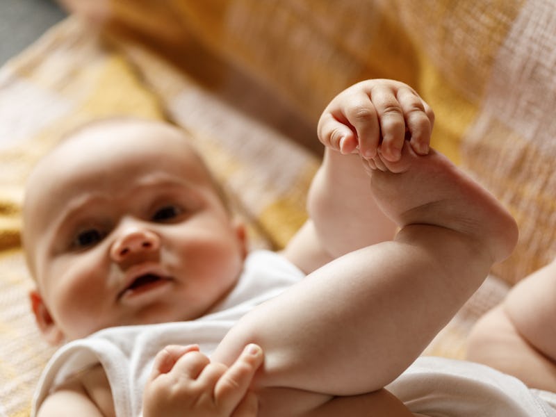 Close up shot of adorable baby boy lying on the sofa, on his back, discovering and playing with his ...