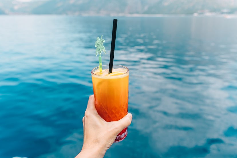 Cocktail Sex on the Beach in human hand on blue sea background. Travel and relax concept.