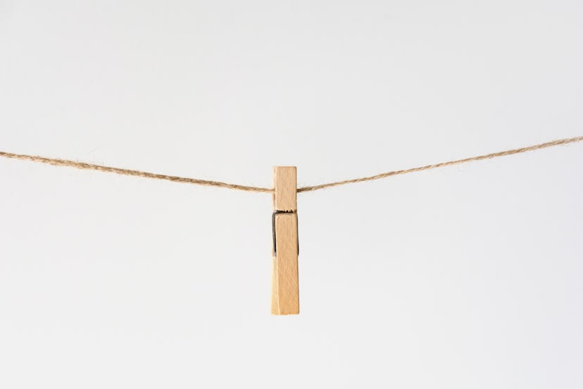 One wooden clothespin hang on rope in center on gray background. Household and Laundry Products. Eco...