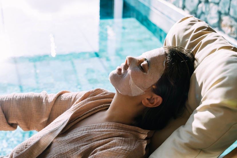Woman in face mask relaxing near the blue swimming pool indoor. Luxury resting on the villa.