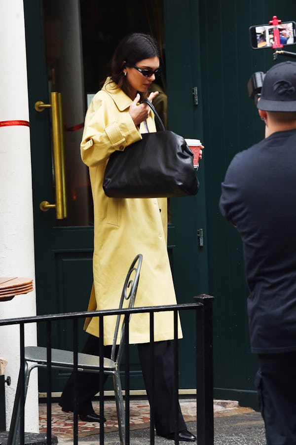 Kendall Jenner wears a tank, trousers, yellow coat, and massive black bag on September 18, 2023 in N...
