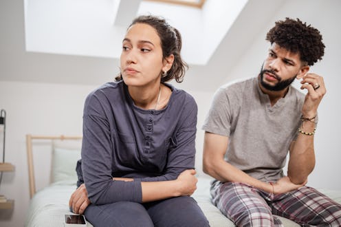A woman and a man in pajamas are sitting side by side on the bed. A man is trying to talk with his g...