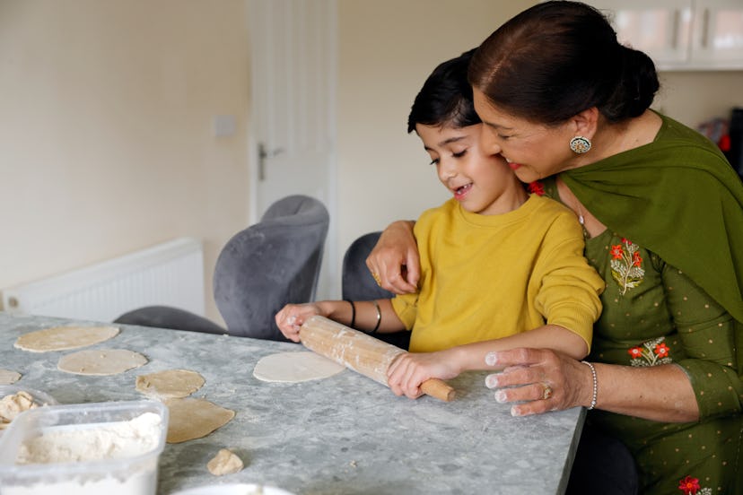 A young boy helping his grandmother roll out some dough at home in the kitchen