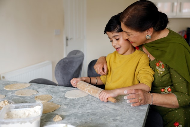 A young boy helping his grandmother roll out some dough at home in the kitchen