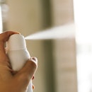 A bottle of white deodorant spray spraying a jet of air in a woman's hand. Woman's hands pushing a b...