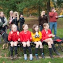 young soccer players sitting on chairs on sideline, parents and families talking and cheering in the...
