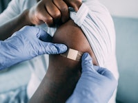 Female doctor putting a bandage on the arm of a male patient after giving Coronavirus/COVID-19 vacci...