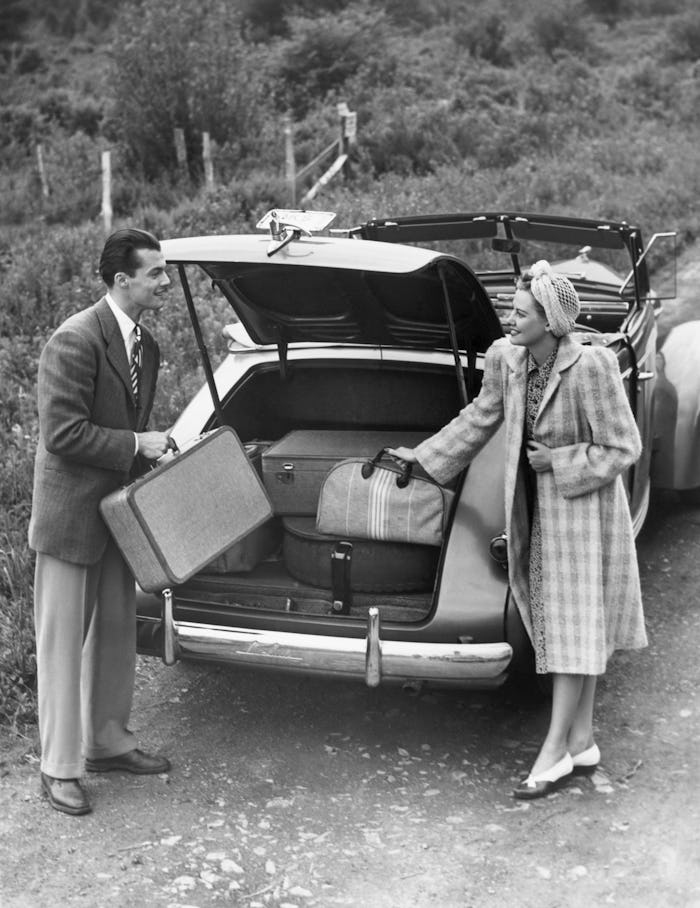 UNITED STATES - CIRCA 1950s:  Couple unloading luggage from trunk of car.