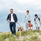 A dad, mom, daughter and son walking their dog on a hill by the sea.