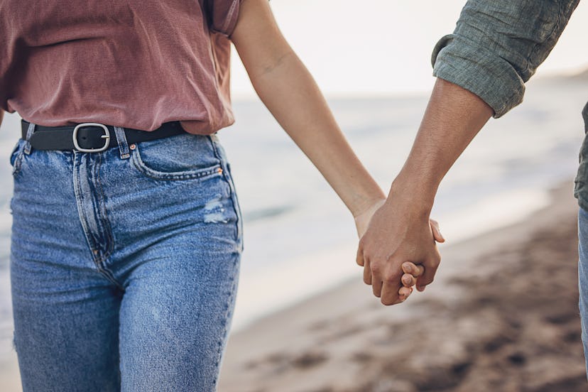 Man and woman holding hands on the beach by the sea.
