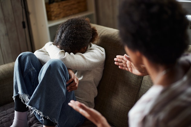 Depressed African American girl crying while relaxing with her single mother on sofa at home.