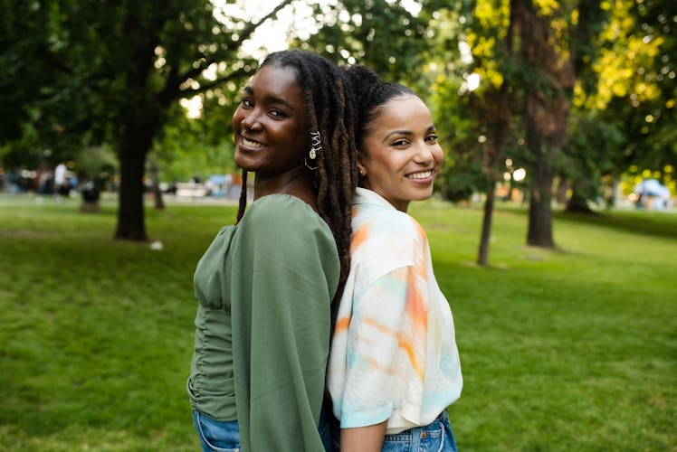 two young women pose with their backs together as they consider the reason why they ghosted someone,...