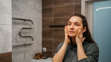 woman using face cream in bathroom at home