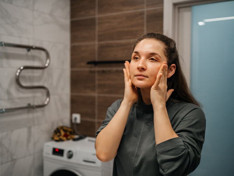 woman using face cream in bathroom at home