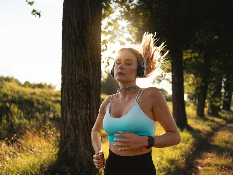 Young active Caucasian woman listening to music on wireless headphones while jogging/running in the ...
