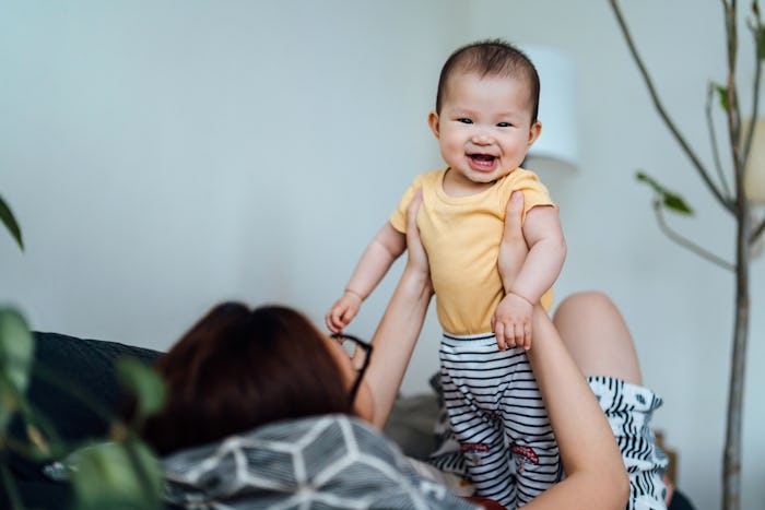 Young Asian mother playing with her adorable baby daughter on sofa at home. Baby girl is smiling and...