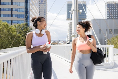 Portrait of cheerful women talking while going to the gym. An African American woman is holding a wa...