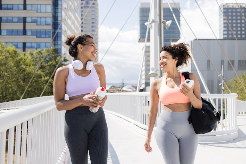 Portrait of cheerful women talking while going to the gym. An African American woman is holding a wa...