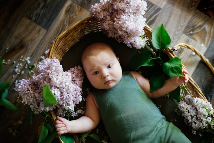 Cute baby in green cotton overalls among lilac flowers. Portrait of newborn in flowers, eco style, n...