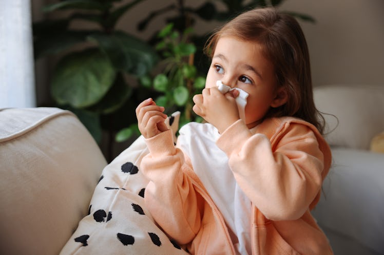 Sick little schoolgirl coughs and blows nose wiping with white paper napkin.