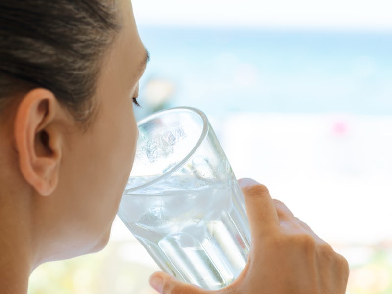 Female is holding glass of water full of ice cubes at the beach.