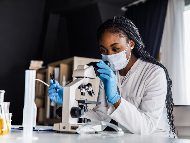 Portrait of serious young female laboratory technician, wearing protective face mask and gloves, loo...