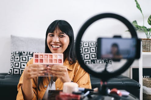 Young woman filming a beauty and makeup vlog for social media content, beauty vlogger showing make-u...
