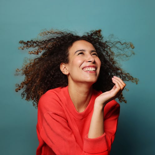 Close-up of beautiful young woman in studio. Female with curly hair laughing, she's wearing a red sw...