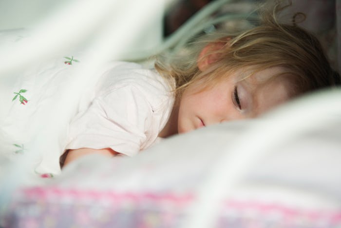 A young child sleeps peacefully on a bed with white and floral bedding.