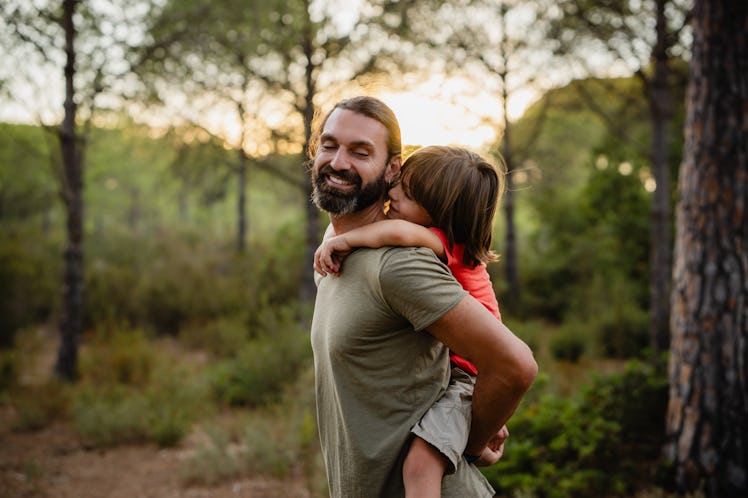 A father and his son on his back look and smile while walking through a forest.