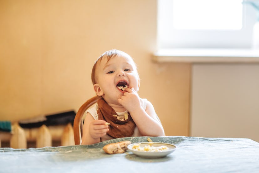 Smiling toddler eats at table from silicone baby plate, in a story explaining why your toddler chews...