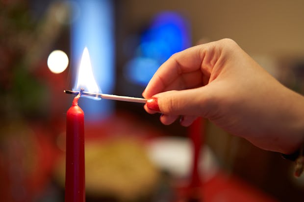 A hand carefully lights a red candle, a symbol of warmth and festivity, against a soft-focus backgro...