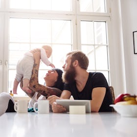 Young tattoed mother and father with newborn baby sitting in their kitchen and having fun together