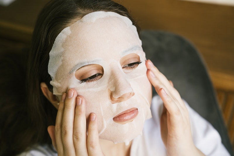 Young woman taking care of her face skin applying face sheet mask at home. Close-up of face. Concept...